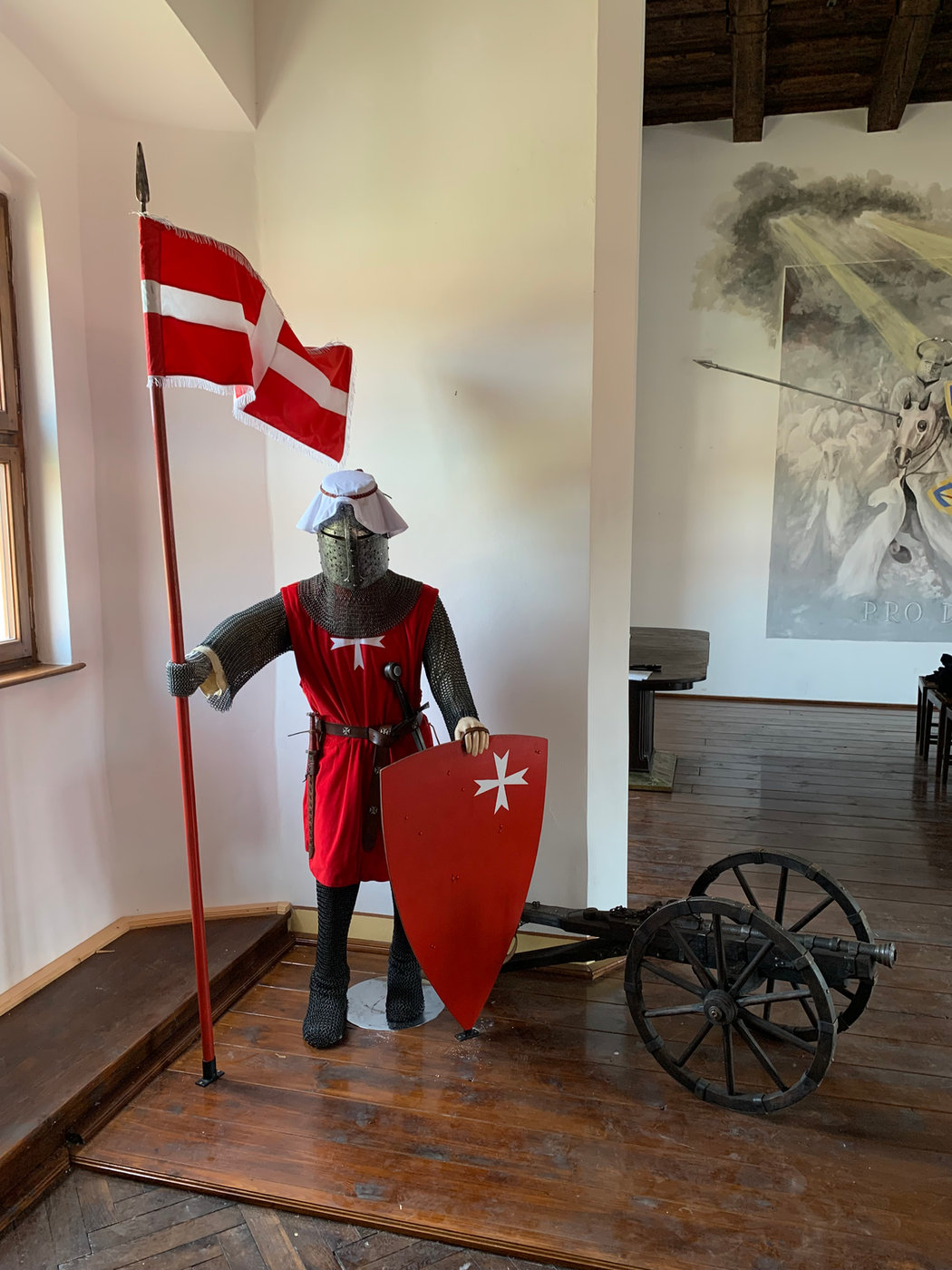 Rytíř ve zbroji s praporem a historickým dělem ve zbrojnici